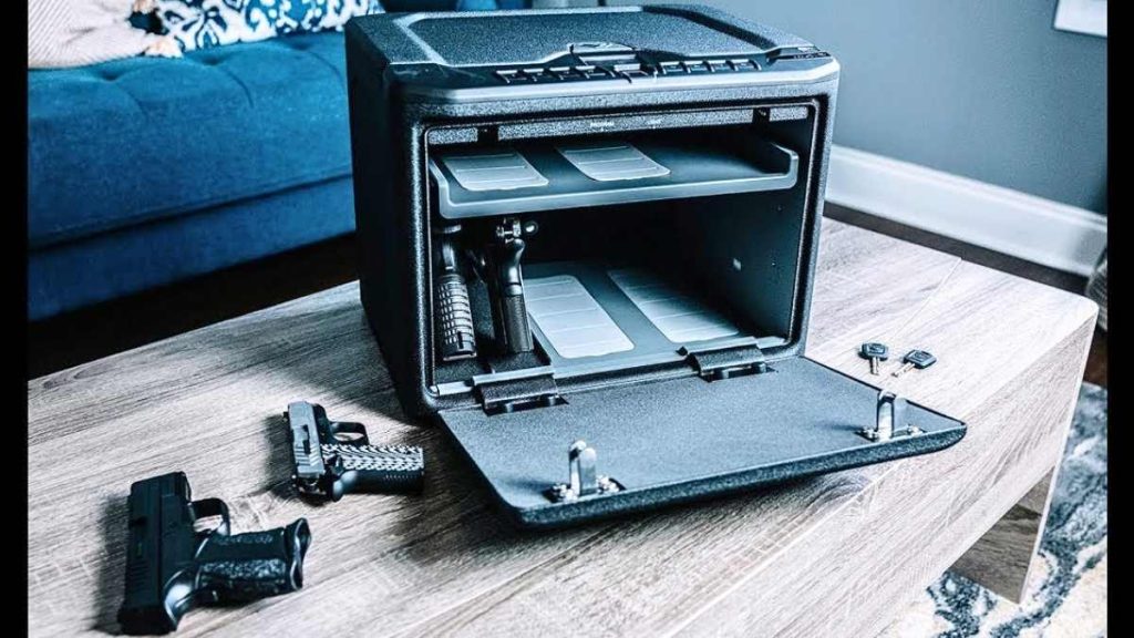 An open VAULTEK MX Series gun safe on a wooden table, displaying two handguns inside and keys beside it, with a blue couch in the background.