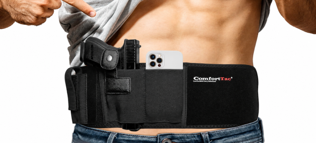 Person wearing a black belly band holster with a handgun and phone tucked inside under a lifted shirt.