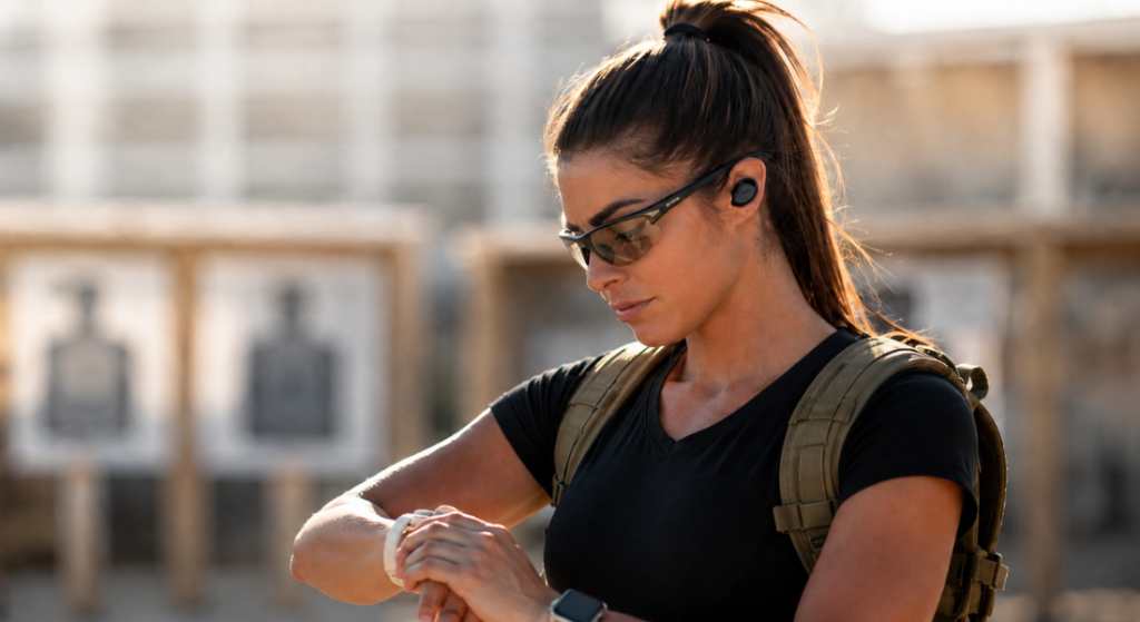 Woman wearing Bluetooth shooting earbuds and safety glasses at an outdoor shooting range.