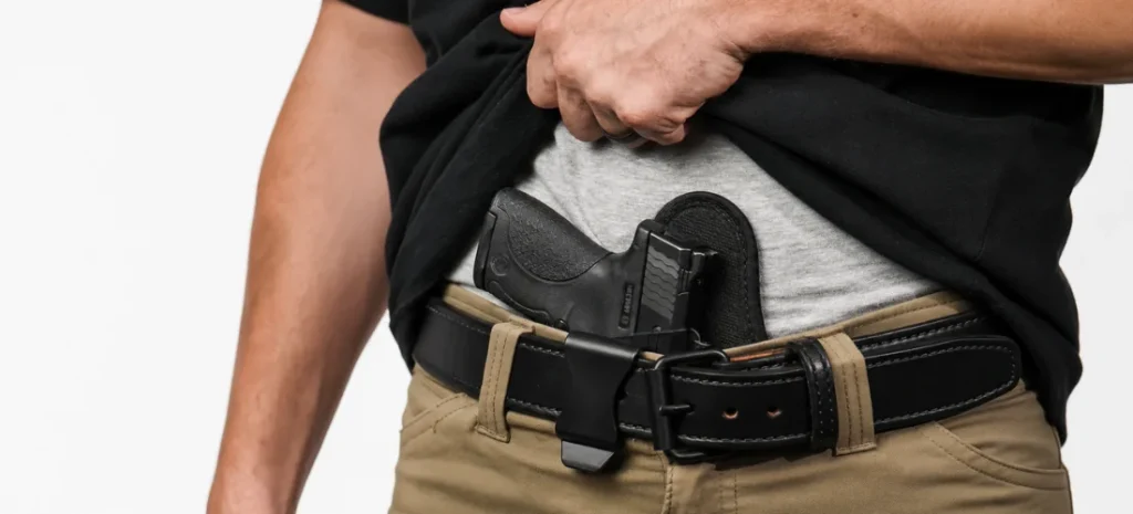 Man carrying a compact handgun in a black appendix holster under a lifted shirt.