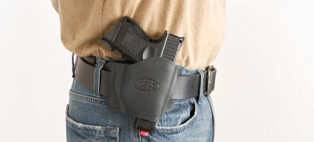 Compact handgun secured in a black leather OWB holster worn with a black belt and blue jeans.