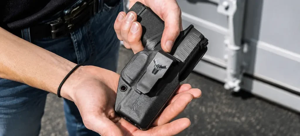 Hands holding a compact handgun in a black holster with a visible logo.