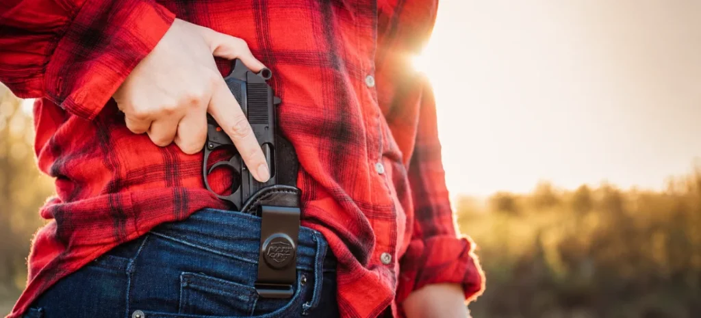 Close-up of a person carrying a handgun in an IWB holster while wearing a red plaid shirt and blue jeans.