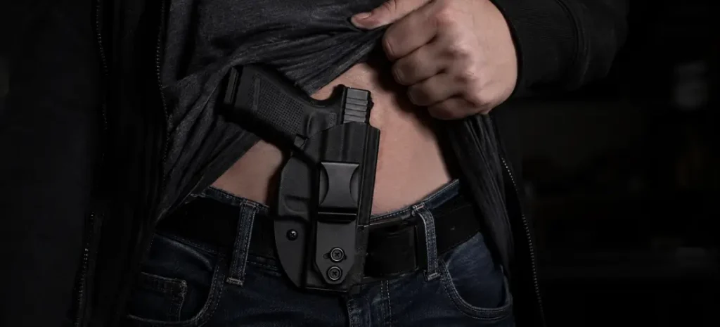 Man carrying a compact handgun in a black IWB holster under a lifted shirt.