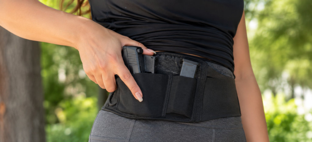 Woman wearing a black belly band concealed carry holster over leggings with a handgun and spare magazine secured at the waist.
