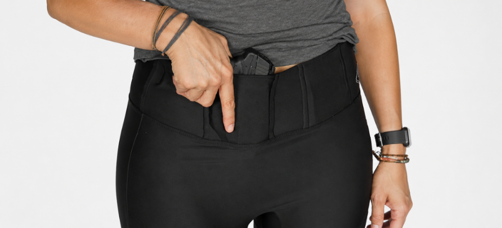 Woman wearing black concealed carry leggings with a compact handgun tucked into the front waistband holster.