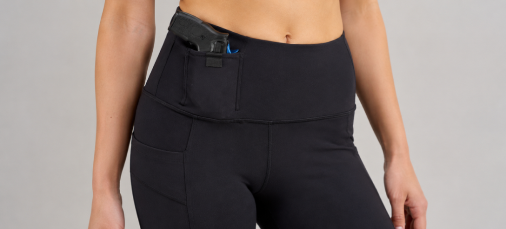Woman wearing black concealed carry leggings with a handgun secured in the front waistband holster pocket.