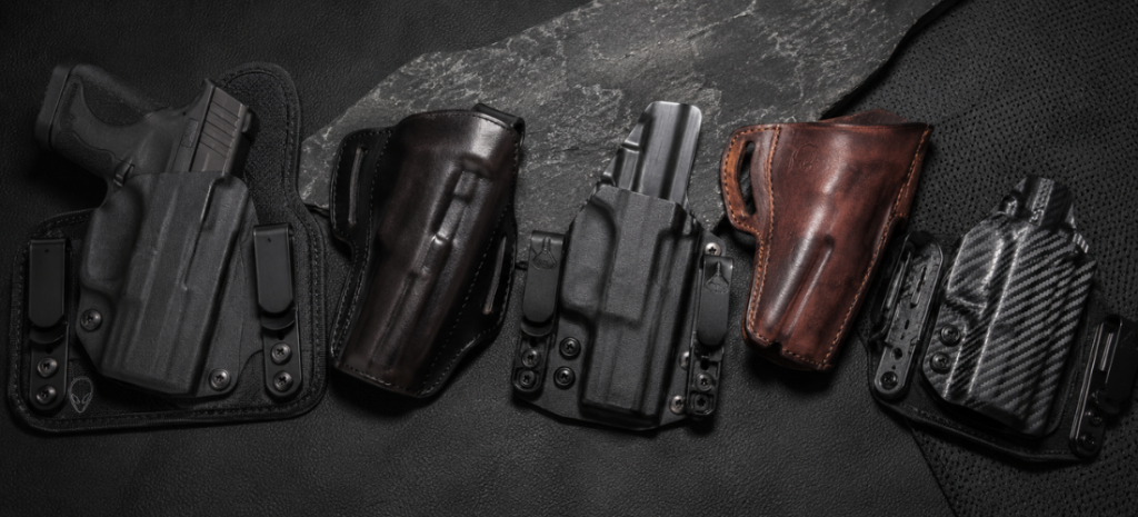 Multiple concealed carry holsters for the S&W Shield arranged on a dark textured surface, including Kydex, leather, and hybrid styles.