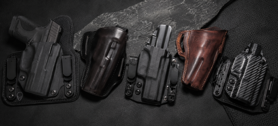 Multiple concealed carry holsters for the S&W Shield arranged on a dark textured surface, including Kydex, leather, and hybrid styles.