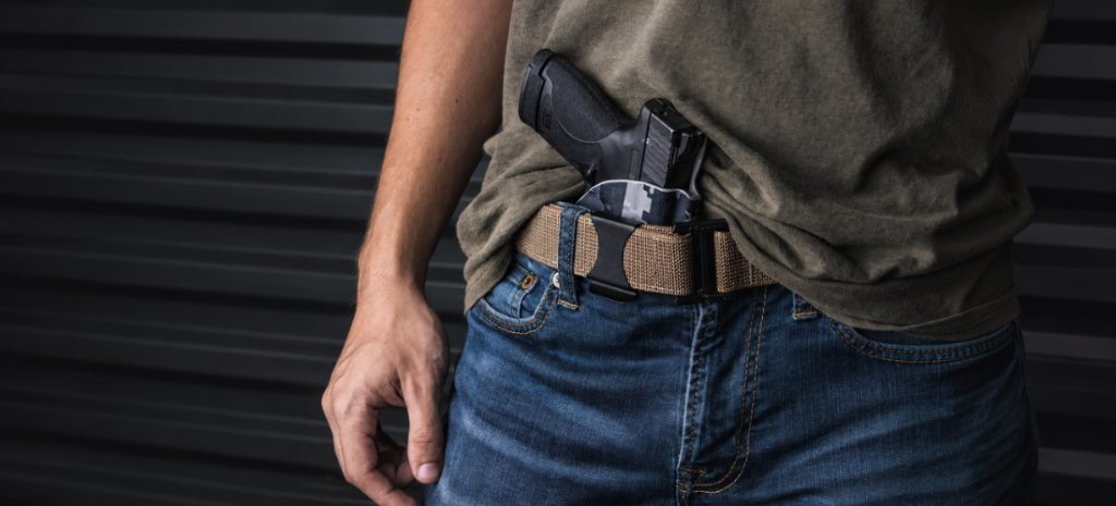 Man carrying a compact handgun in an appendix holster with a tactical belt and jeans.
