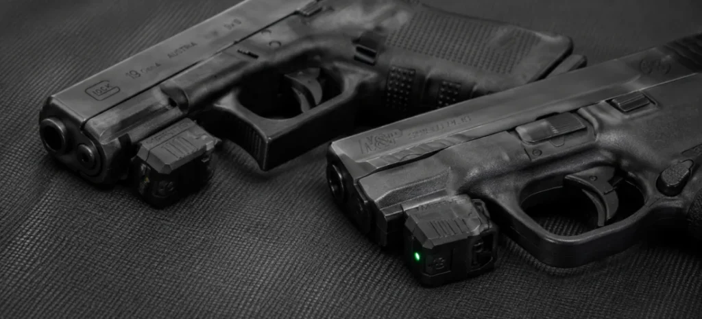Mantis X3 and X10 Elite training sensors mounted beneath two unloaded pistols on a dark shooting mat.