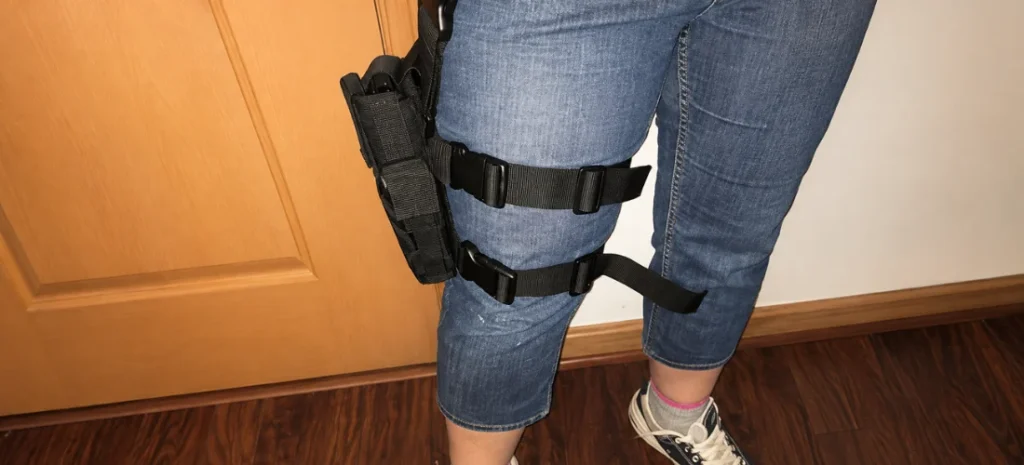 Close-up of a person wearing a black thigh holster with two adjustable straps over blue jeans.