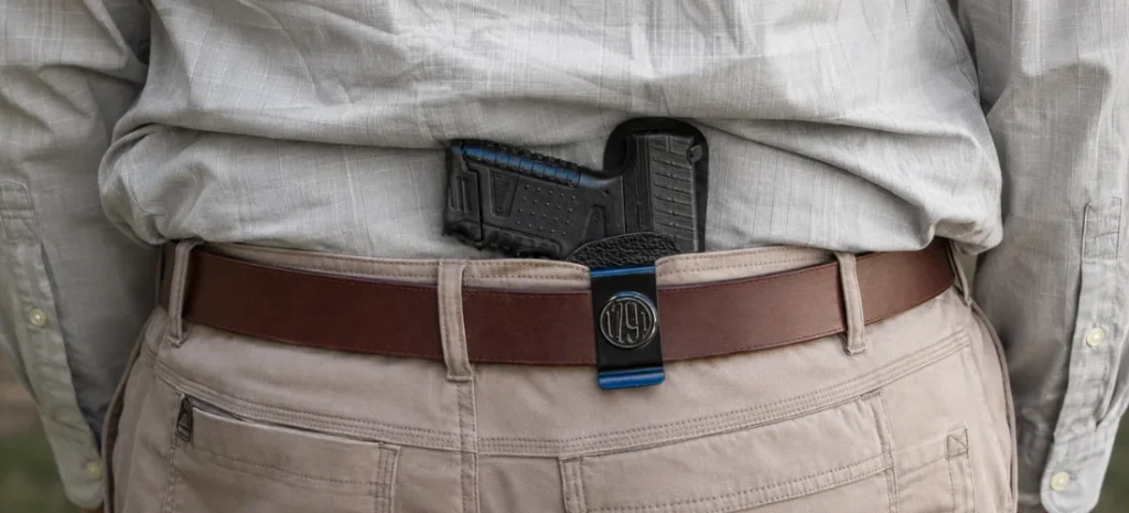 Rear view of a compact handgun secured in an IWB holster beneath a gray shirt and brown leather belt.