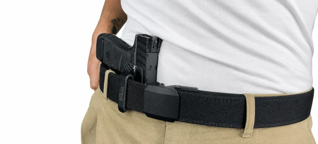 Compact black handgun secured in an IWB holster on a tactical belt worn with khaki pants.